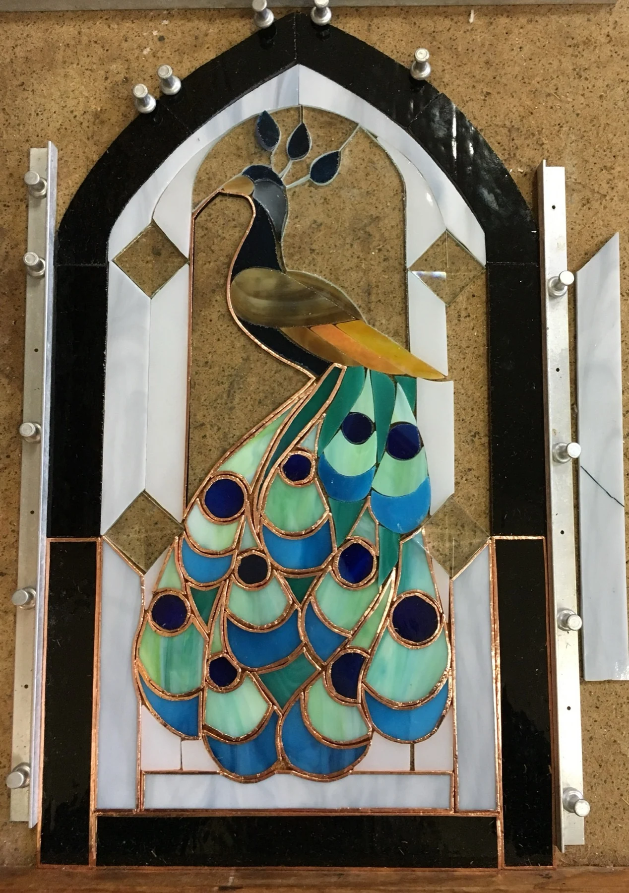 Peacock glass pieces arranged within an arched pattern on a workbench