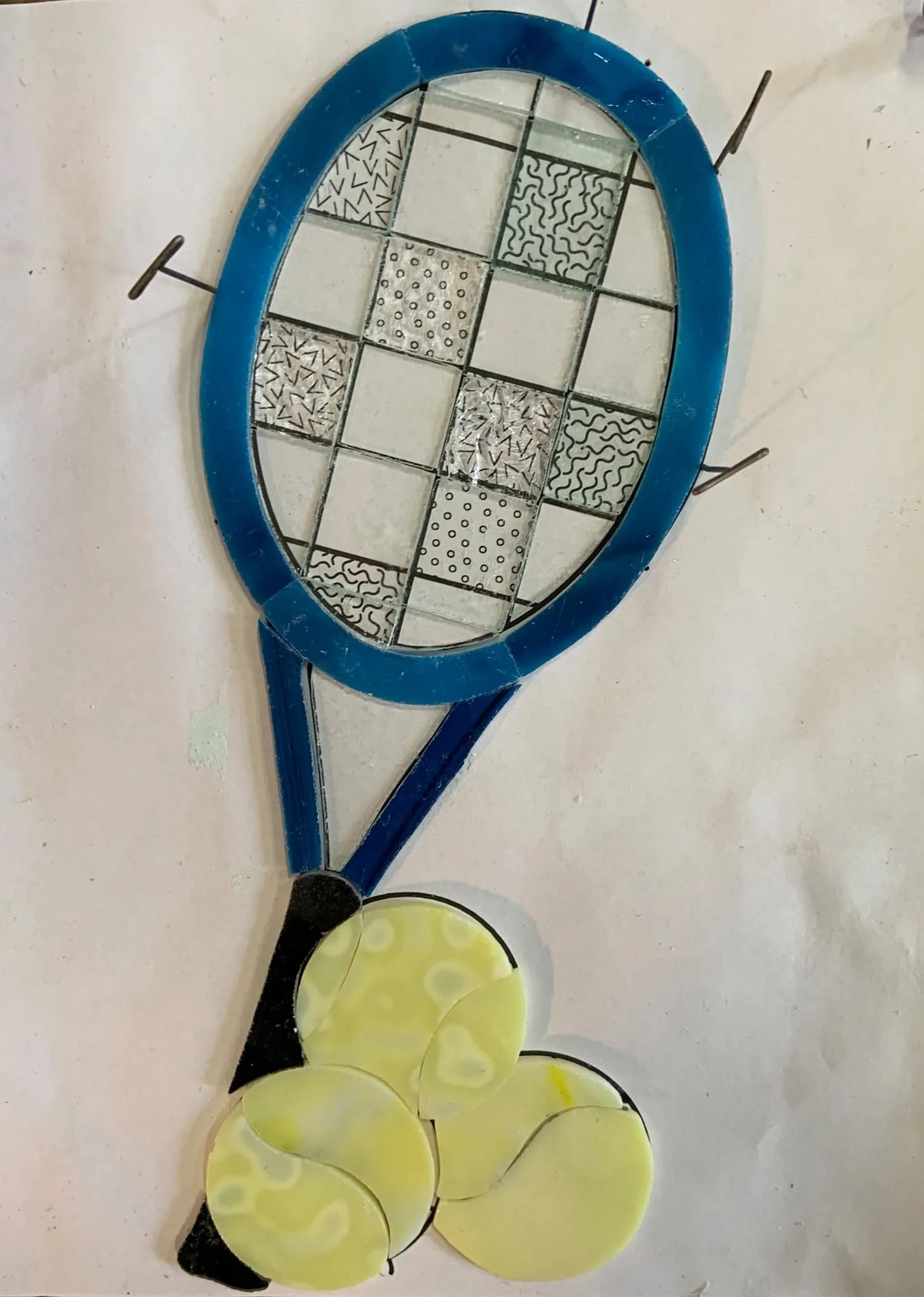 Blue tennis racket and yellow tennis balls laid out on a pattern with pins visible